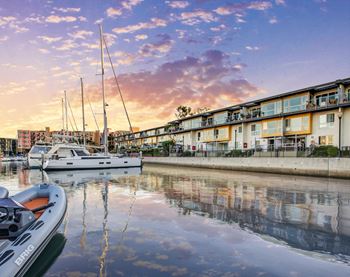 A marina with boats docked in front of a building with a sunset in the background.